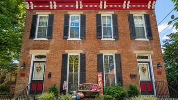 A two-story brick building with a red roof, black shutters, and a bench in front.