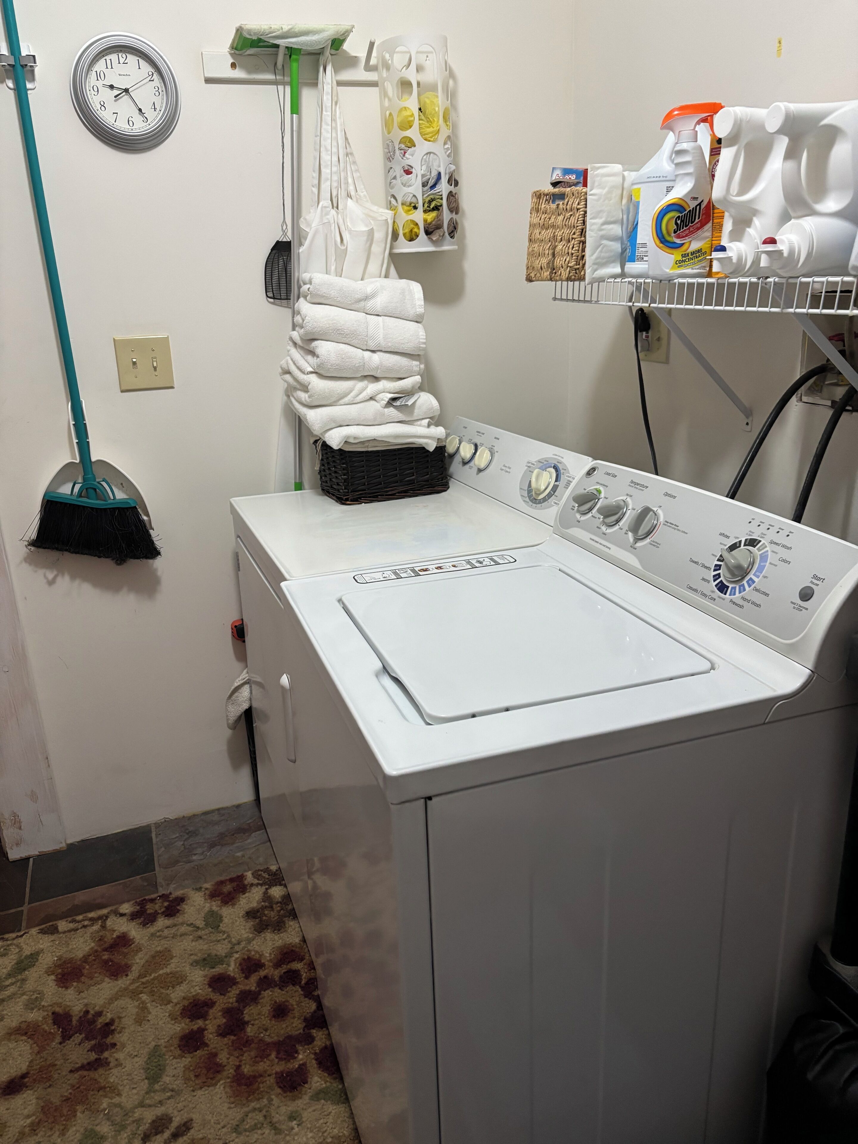 A laundry area with a washing machine, a clock, and various cleaning supplies.