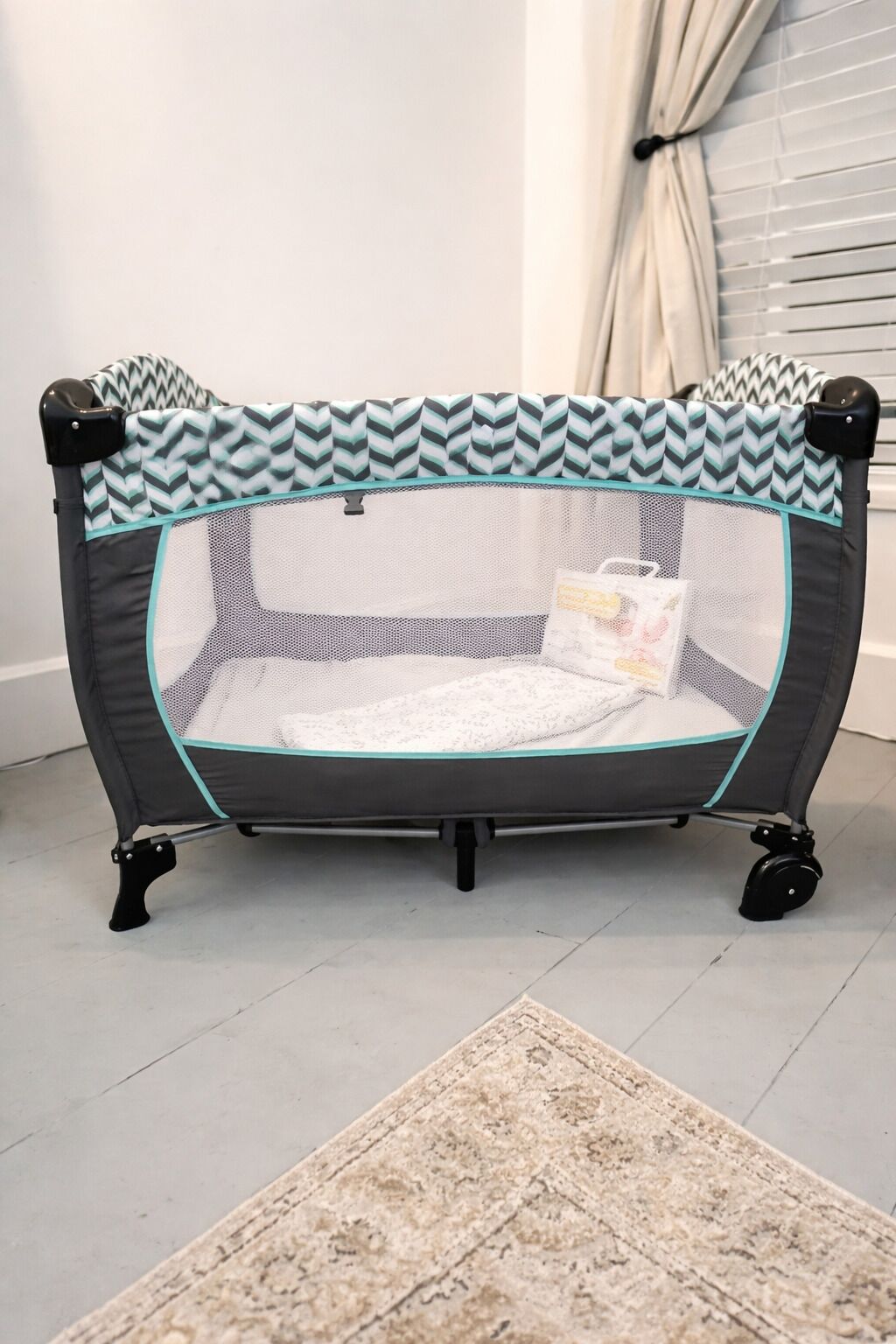 A portable playpen with a chevron-patterned top, a mesh side, and a cushioned bottom.