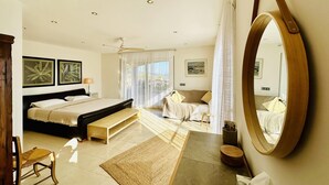 Een moderne slaapkamer met een groot bed, een houten bankje, een tafeltje en een spiegel.
