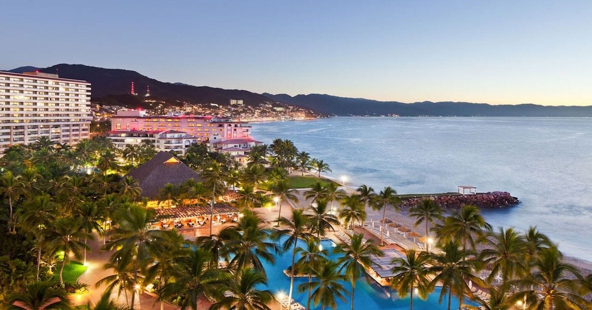Un complexe hôtelier doté d’une grande piscine, de palmiers et offrant une vue sur la plage.