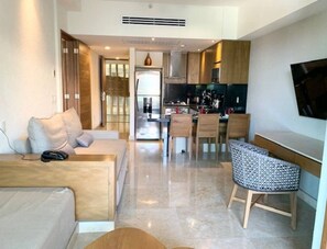 A modern living room with a sofa, a dining area with chairs, and a kitchen in the background.