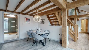 Een eetgedeelte met een houten plafond, een gedekte eettafel met stoelen en een trap naar een hoger niveau.