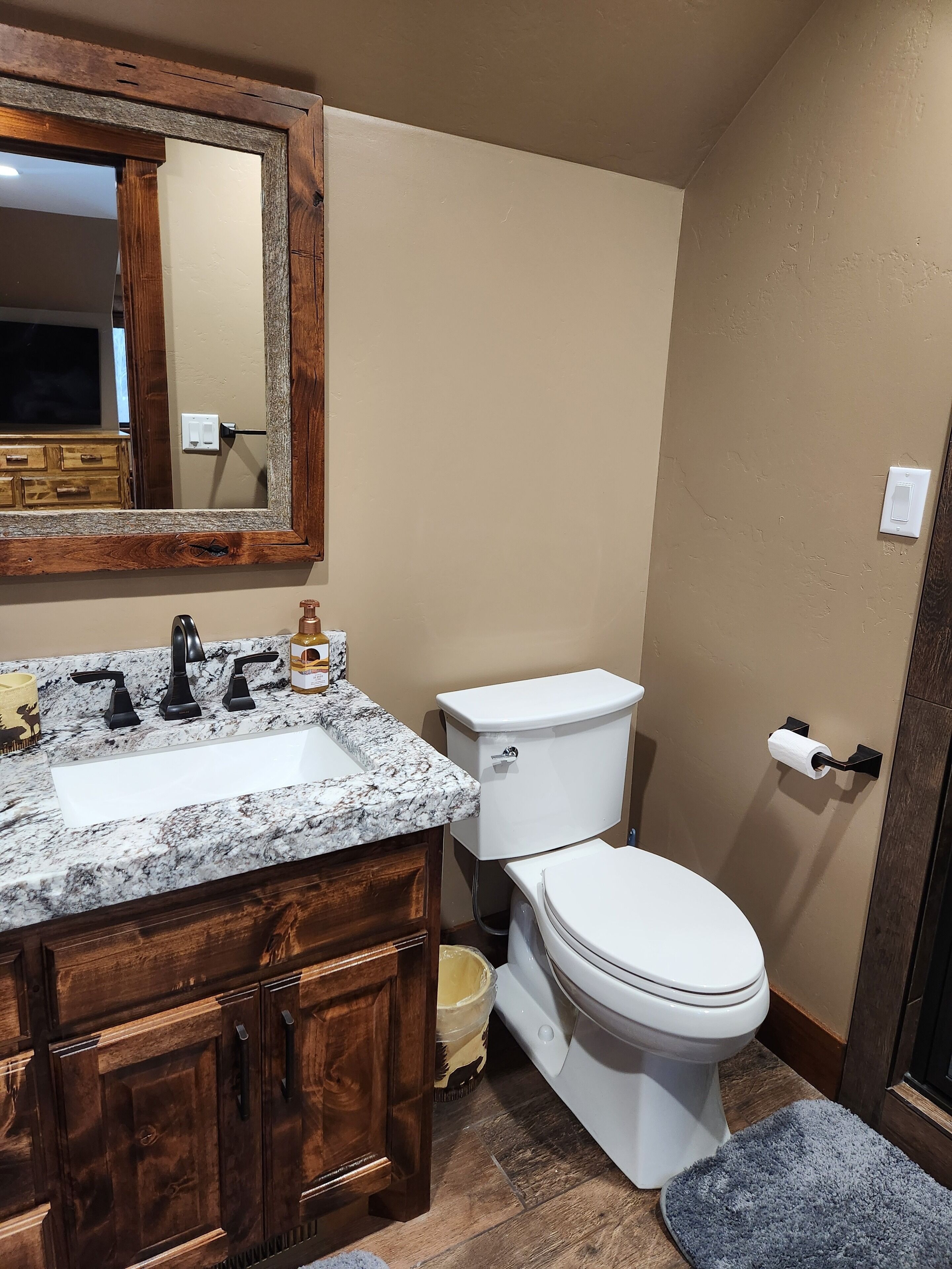 Une salle de bain avec un lavabo en marbre, un meuble-lavabo en bois, des toilettes blanches et un grand miroir.
