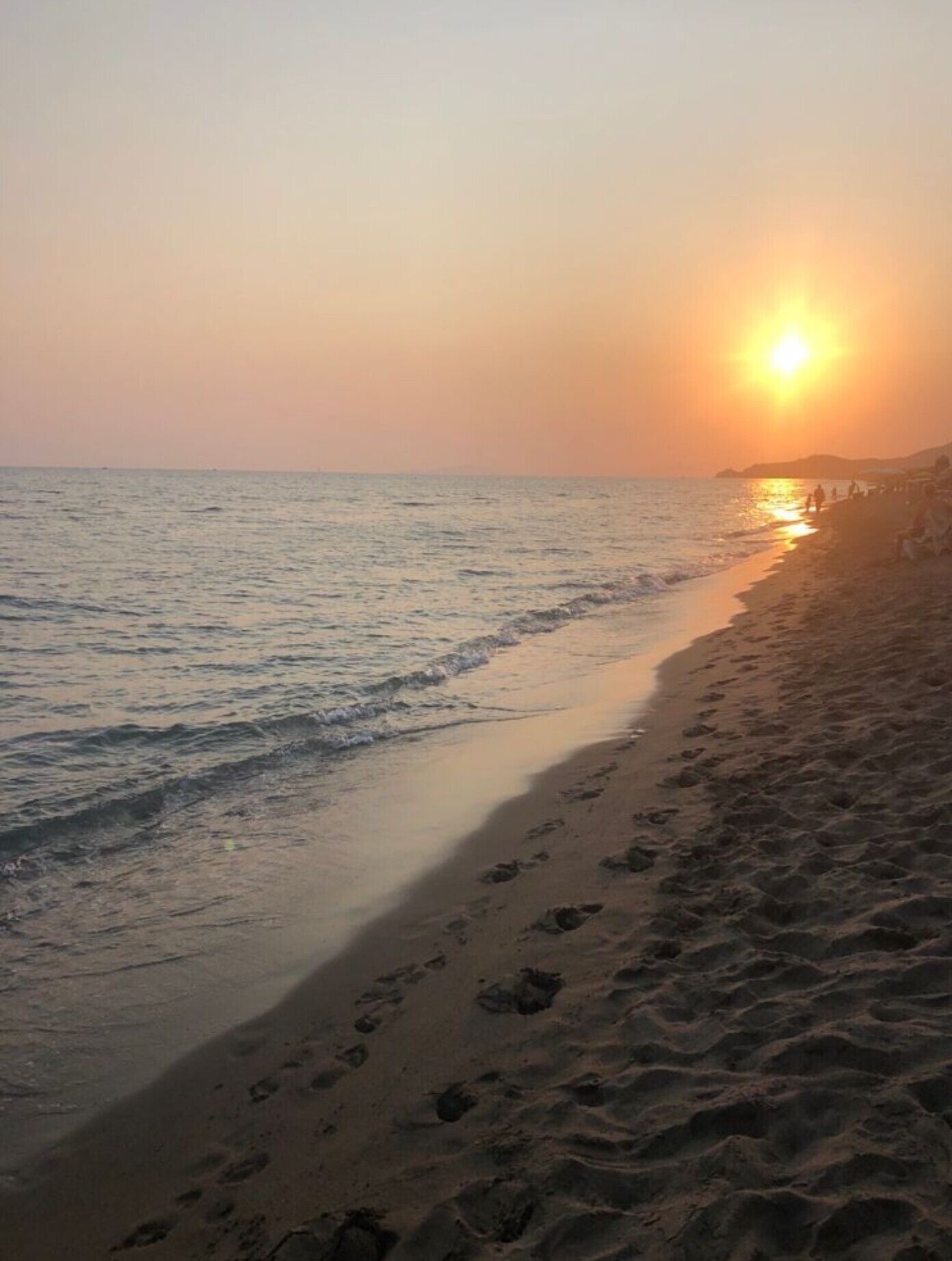Ein Strand mit Fußspuren, die zum Wasser führen, ein Sonnenuntergang im Hintergrund und ein klarer Himmel.