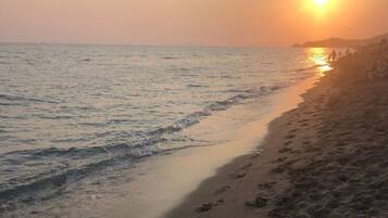 Ein Strand mit Fußspuren, die zum Wasser führen, ein Sonnenuntergang im Hintergrund und ein klarer Himmel.