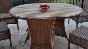 Una mesa redonda de madera con sillas de mimbre, un cuenco de fruta y vistas a colinas ondulantes.
