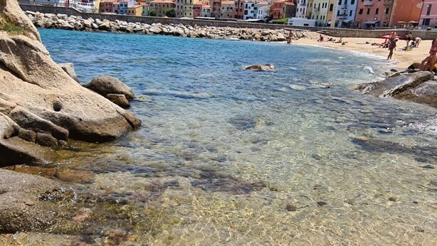 Un pueblo costero con aguas cristalinas, costa rocosa y edificios coloridos.