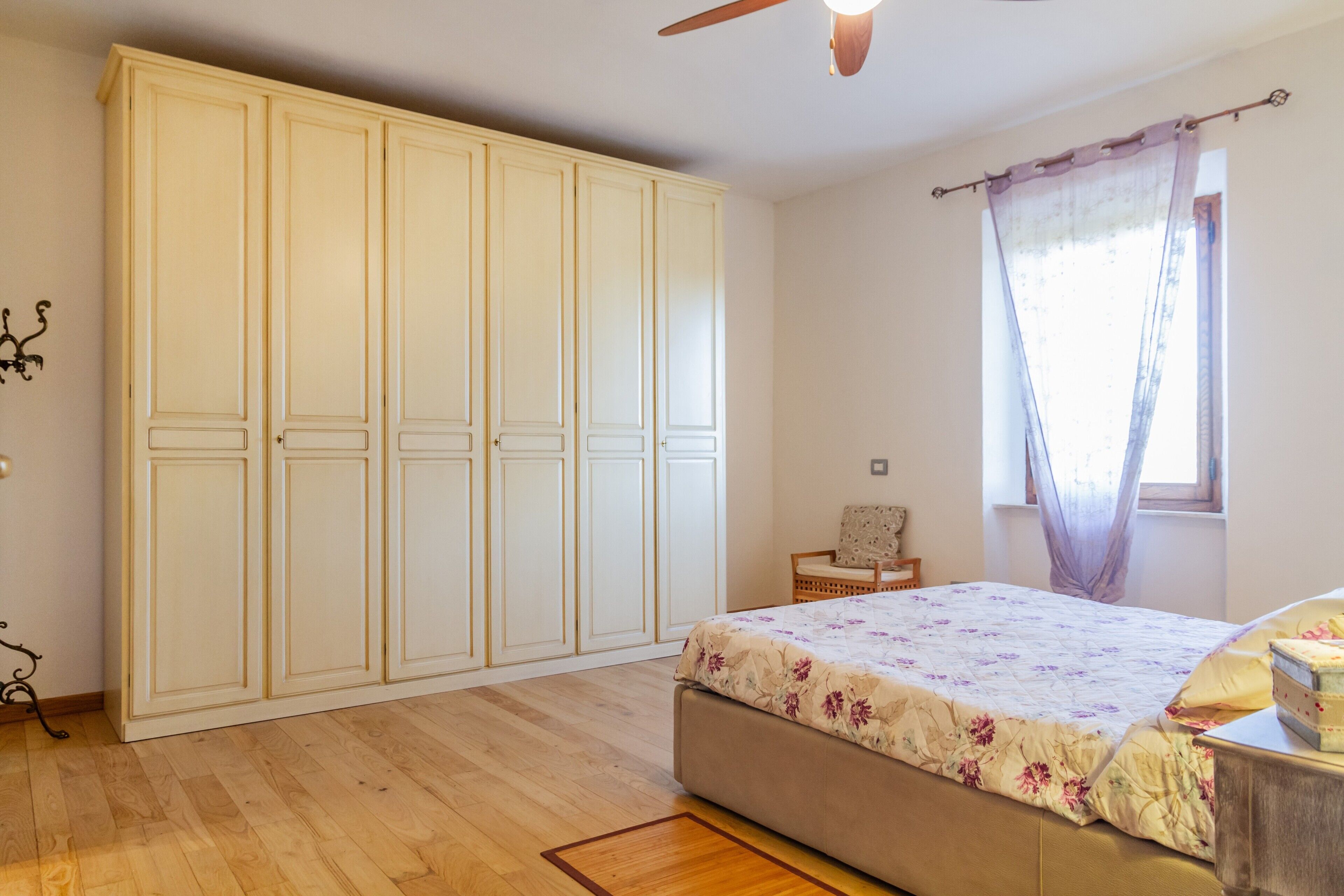Une chambre à coucher avec un lit, une armoire, une fenêtre avec des rideaux et un ventilateur de plafond.