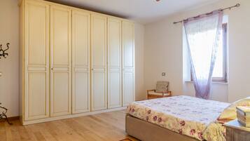 Une chambre à coucher avec un lit, une armoire, une fenêtre avec des rideaux et un ventilateur de plafond.