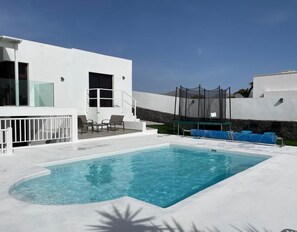 A modern pool area with a rectangular pool, white walls, and a covered seating area with chairs.