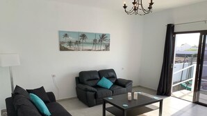 Ein modernes Wohnzimmer mit einer schwarzen Couch, einem schwarzen Sessel und einem Couchtisch. An der Wand hängt ein Gemälde mit einer Strandansicht.