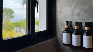 Ein Zimmer mit Fensterblick auf eine Landschaft, einer Betonwand und drei Shampooflaschen an der Wand.
