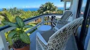 Un balcone con sedie in vimini bianco e un tavolino, con vista su un paesaggio costiero con palme e l'oceano.