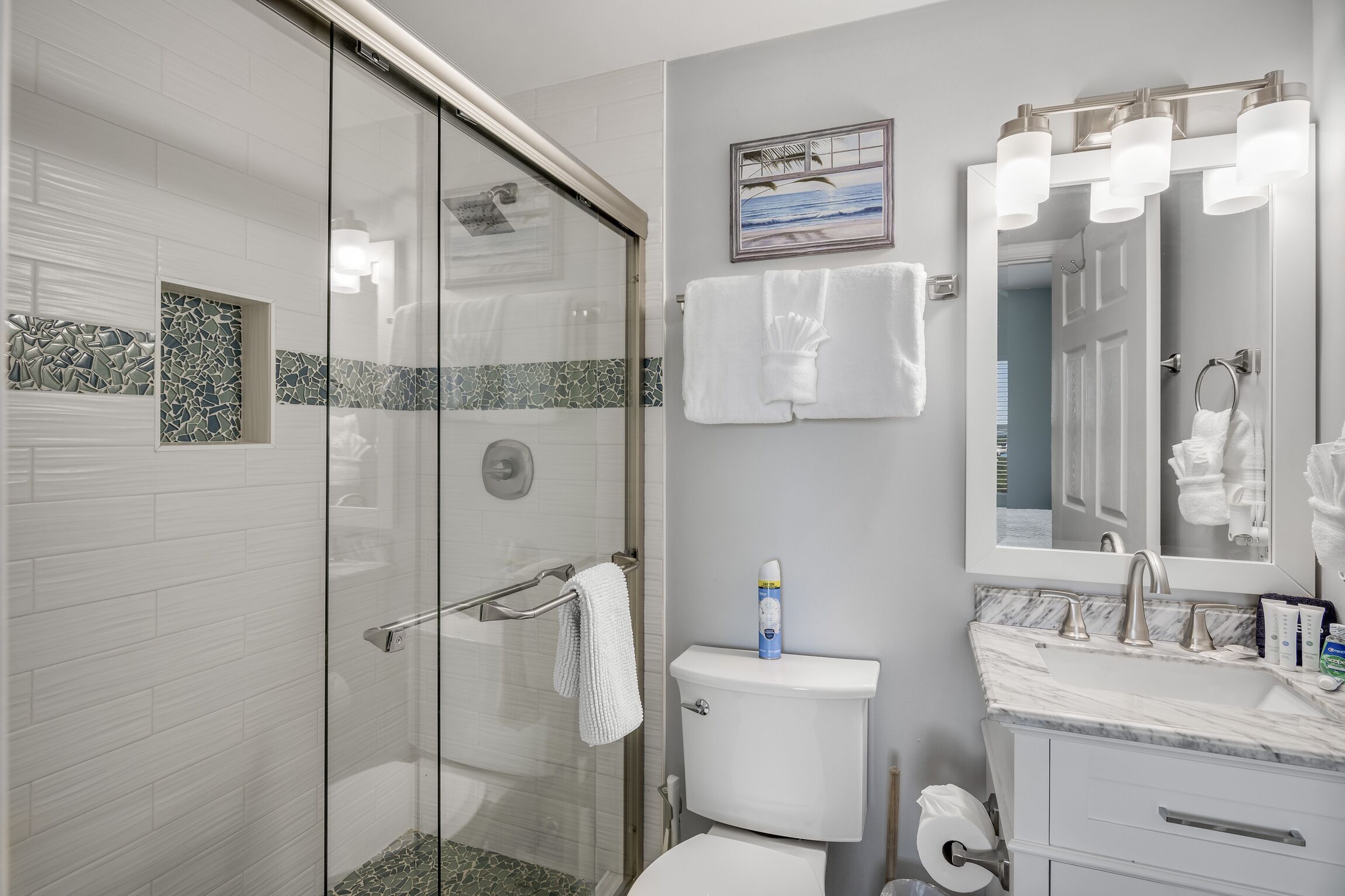 Un baño moderno con cabina de ducha de vidrio, inodoro, lavabo con encimera de mármol y espejo con iluminación.