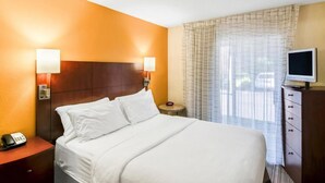 Een hotelkamer met een bed, bedlampen, een televisie, een telefoon en een raam met gordijnen.
