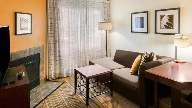 Een hotelkamer met een bank, een kleine tafel, een lamp, een openhaard en lijstjes met foto's aan de muur.