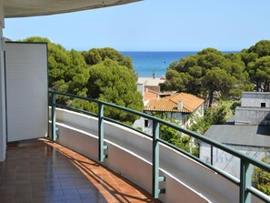 Un balcón con vista al mar, árboles y edificios.