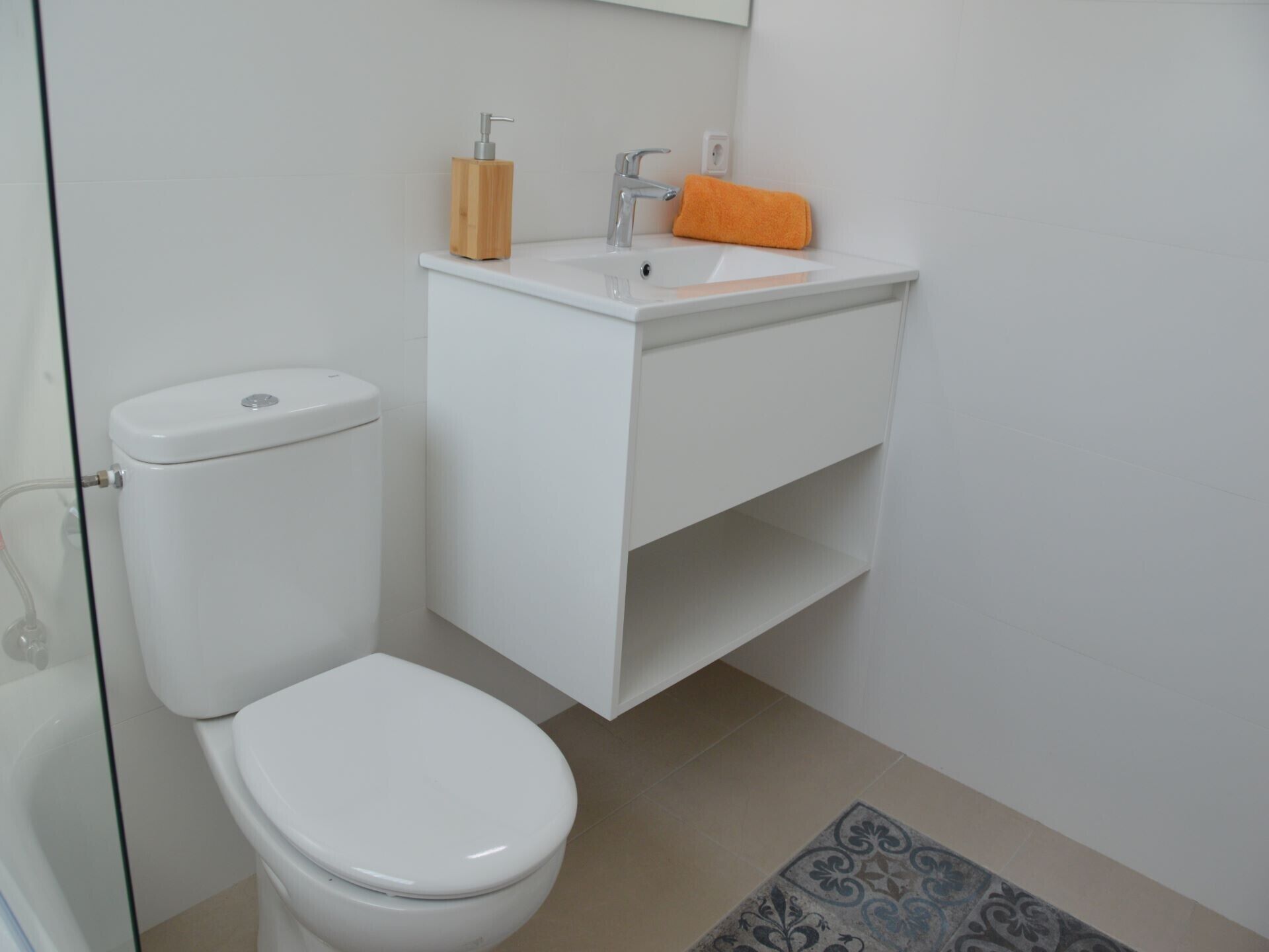 A small, modern bathroom with a toilet, sink, and a glass shower enclosure.