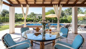 Un espace extérieur abrité, doté d’une table en verre, de chaises et offrant une vue sur une piscine.