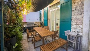 Eine Terrassengruppe im Freien mit Holztisch und Bänken, einem Grill und einer Steinmauer.