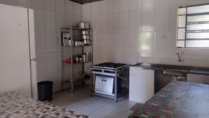 A kitchen with a tiled floor, a stove, a sink, and a shelf with pots and pans.