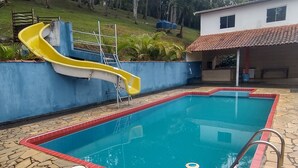 A rectangular swimming pool with a yellow slide, surrounded by a stone and brick deck.