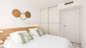 A bedroom with a bed, white bedding, a wooden headboard, a white door, and a wall-mounted circular decoration. - Palazzio Re-2753-Modern apartment close to the Port (Cannes)