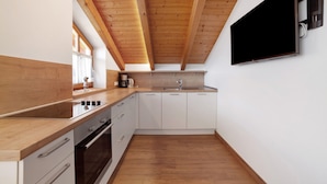 Een moderne keuken met houten balken, een inbouwoven, witte kastjes en een aan de muur bevestigde televisie.