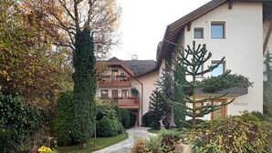 A residential area with a pathway leading to a house with a balcony, surrounded by various plants and trees.