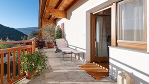 A balcony with a wooden railing, a chair, potted plants, and a view of the mountains.
