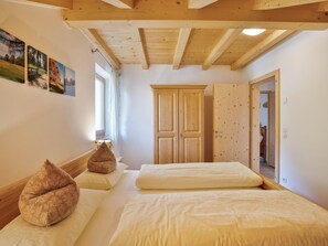 A bedroom with two beds, wooden ceiling beams, a wardrobe, and a window with curtains.
