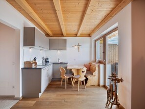 A modern kitchen with wooden beams, a dining area with a wooden table and chairs, and a large window.