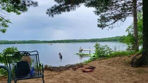 Una platja sorrenca amb una cadira de metall i un petit moll que s'endinsa en un llac.