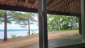 Vista des de l'interior d'una cabana amb sostre de fusta i grans finestres que donen a una zona de llac amb arbres i un tobogan.