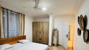 A bedroom with a bed, a wardrobe, and a door leading to another room. - Charming & Spacious Apt in Accra (Accra)