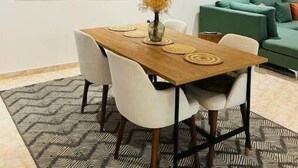 A dining area with a wooden table, white chairs, and a woven pendant light. There are abstract paintings on the wall and a green sofa in the background. - Charming & Spacious Apt in Accra (Accra)