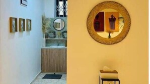 A hallway with a tiled floor, a round mirror on the wall, a small table, and a window with decorative bars. - Charming & Spacious Apt in Accra (Accra)
