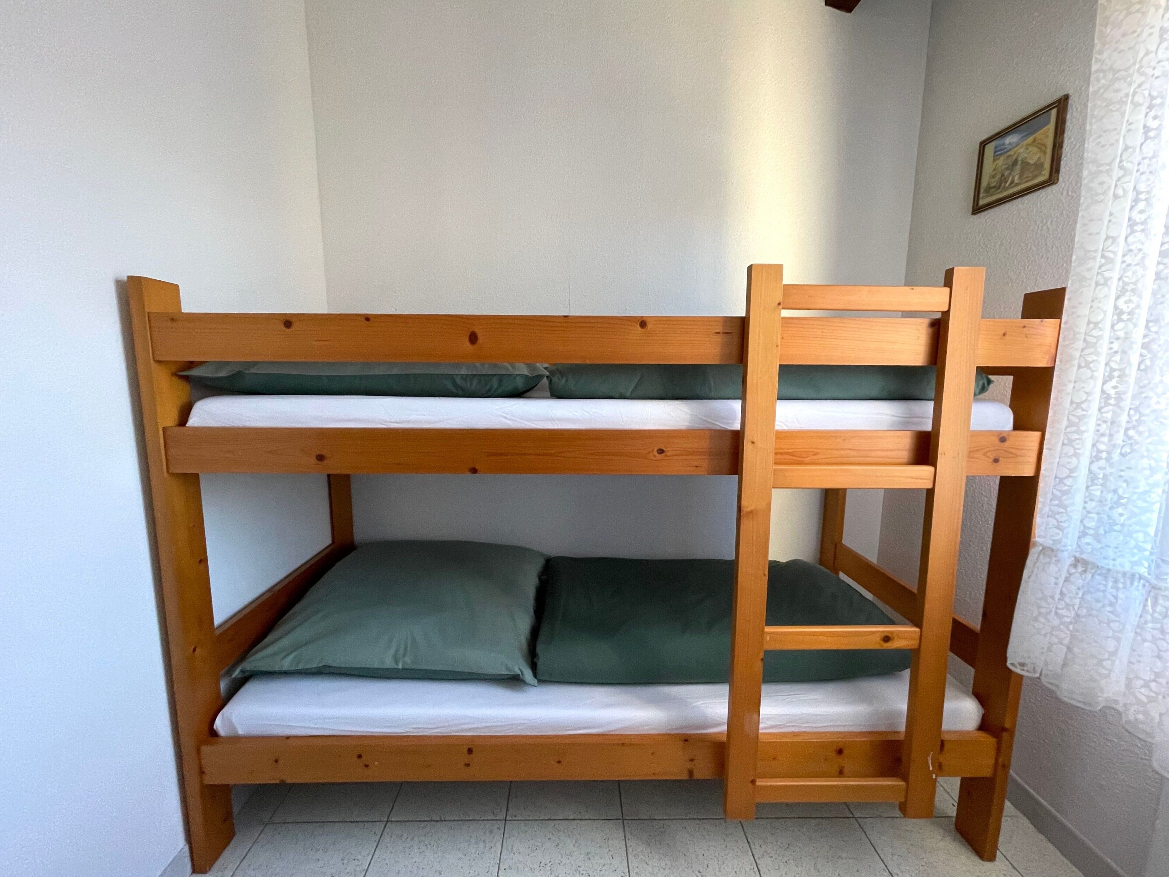Een stapelbed met twee niveaus, houten frame en groene beddengoed.