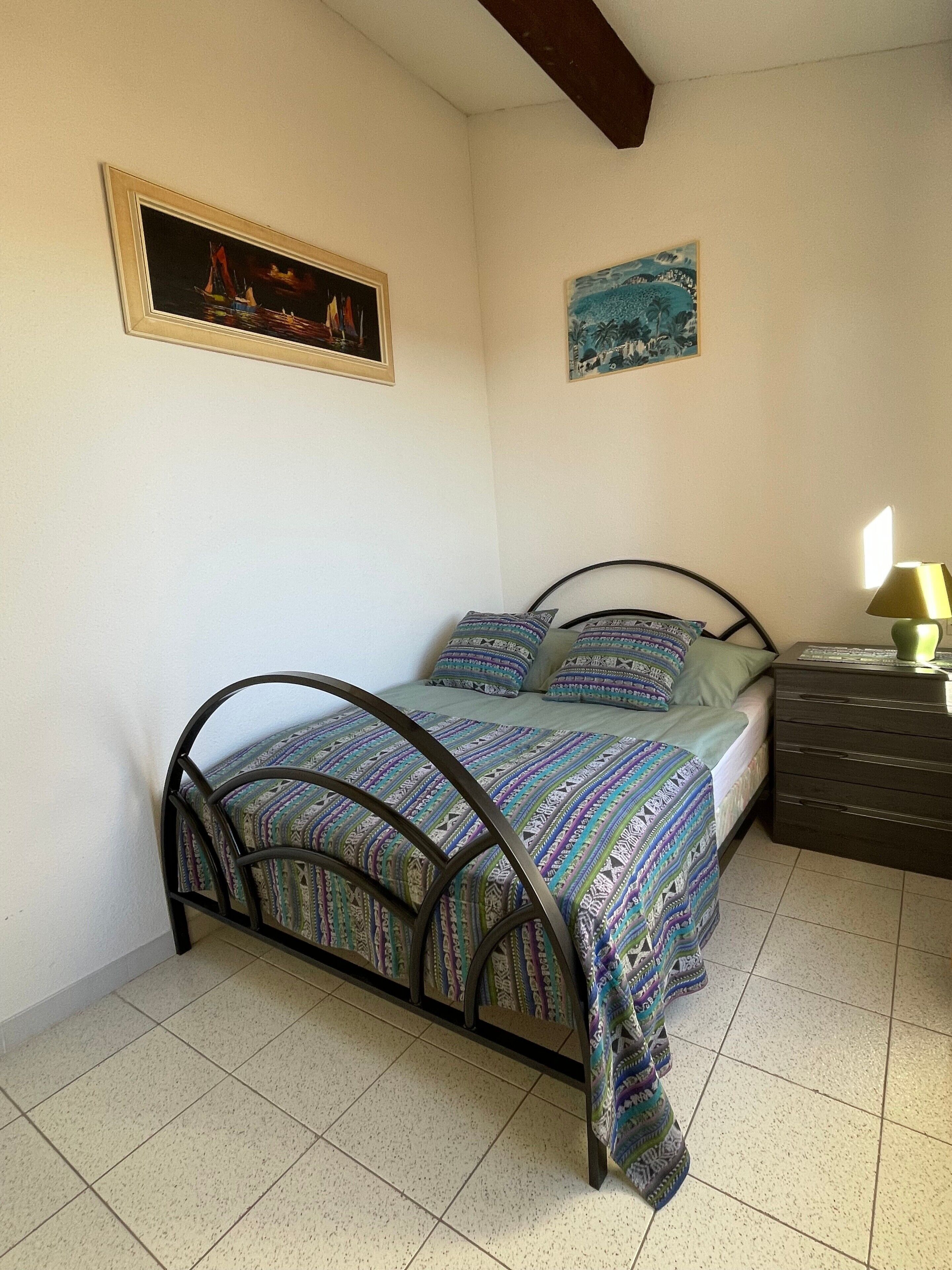 Een slaapkamer met een bed, een kaptafel, een lamp en twee schilderijen die aan de muur hangen.