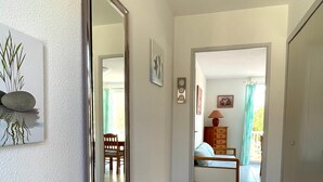 A hallway with a large mirror, a bench, a bed, and a dresser in the adjacent room.