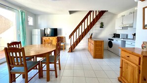 A kitchen with wooden cabinets, a dining table with chairs, a washing machine, and a staircase.