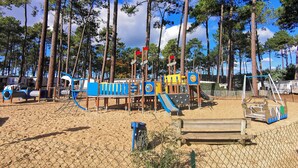 Une aire de jeux avec des structures d’escalade et des toboggans, entourée de grands arbres et surplombée par un ciel dégagé.