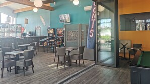 Un espace bar avec des tables, des chaises, des jeux d’arcade et une table de billard.