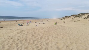 Une plage de sable où l’on voit des gens et des parasols, un ciel dégagé et une pente douce qui descend vers l’eau.