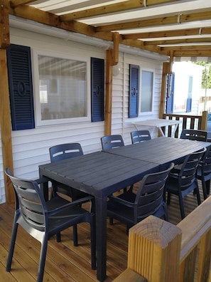 An outdoor patio with a wooden pergola, a table with chairs, and windows with shutters. - Mobile Home 'Du Soleil - Contis' with Shared Pool, Terrace and Fun Pass Included (Saint-Julien-en-Born)