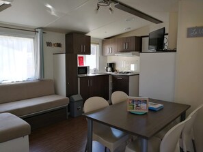 A compact RV interior with a kitchenette, a dining area, and a seating area. - Mobile Home 'Du Soleil - Contis' with Shared Pool, Terrace and Fun Pass Included (Saint-Julien-en-Born)