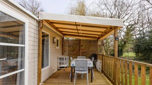 A covered patio with a table and chairs, a wooden deck, and a view of the surrounding landscape.