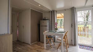 A modern kitchen with a refrigerator, a dining table with chairs, and a view of the outdoors through a glass door.