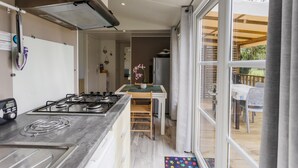 A modern kitchen with a gas stove, a microwave, and a built-in oven. There is a dining area with a table and chairs, and a view of an outdoor deck through a large window.